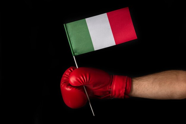 Boxer hand holds flag of Italy. Boxing glove with the Italian flag. Black background.