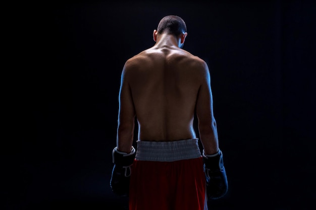 A boxer in his shorts stands with his back his head is lowered recreation black background