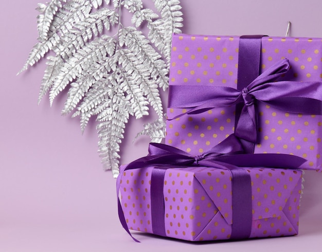 Boxes packed in festive purple paper and tied with silk ribbon on a purple background, gift, surprise