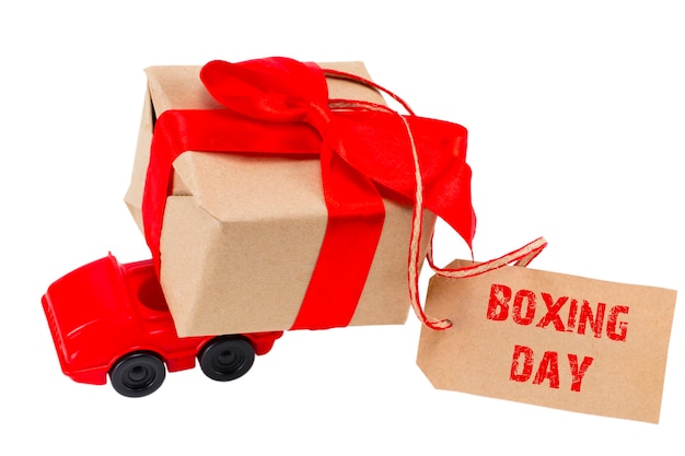 Il concetto di boxing day. macchinina rossa che consegna scatola di regali con etichetta con testo: boxing day su sfondo bianco.