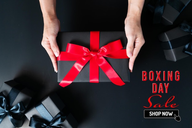 Photo boxing day sale, woman hand give the gift box on black background