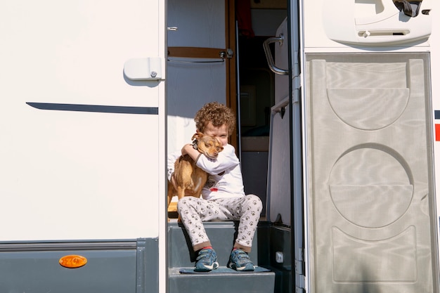 Boy of 45 years Caucasian sitting in the motor home entrance in pajamas with his little puppy hugging him with affection and love