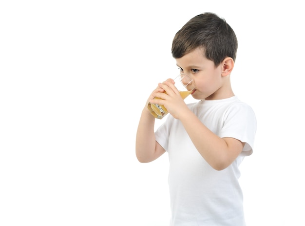 Foto il bambino di 6 anni in una maglietta bianca beve il succo di agrumi su una priorità bassa bianca. sfondo isolato.