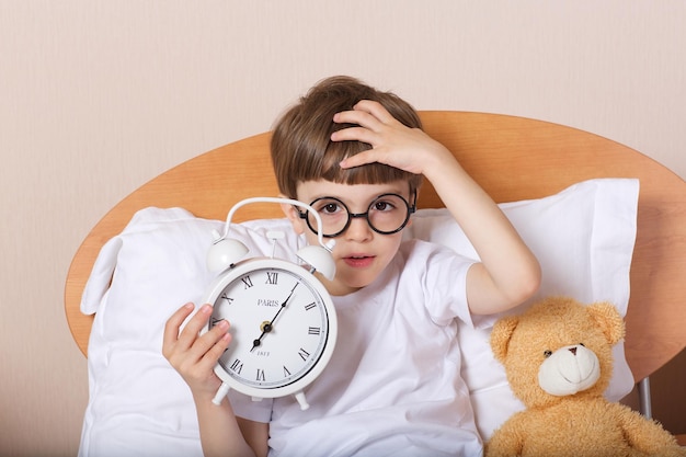 Boy of 6 years old in the bed with big alarm clock