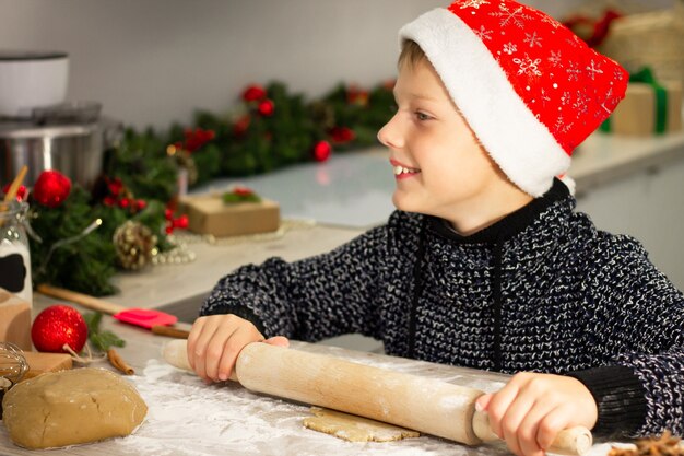 Boy 7-10 in a Christmas Santa's cap, making Christmas gingerbread cookies in the New Year's kitchen.