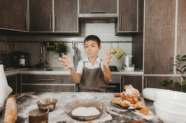 Мальчик 8 лет на кухне играет с мукой. ребенок на кухне готовит тесто.