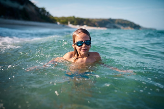 Boy of 8 years old swims in the sea in blue swimming goggles in the evening