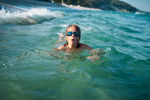 Boy of 8 years old swims in the sea in blue swimming goggles in the evening