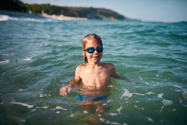 Boy of 8 years old swims in the sea in blue swimming goggles in the evening