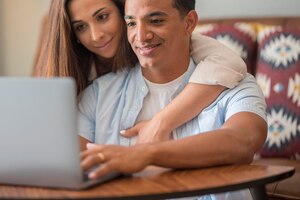 家で一緒にノートパソコンを使う男の子と女の子 座ってウェブを楽しむ 若いカップルの異人種間の人々 コンピューターで作業し、笑顔 人々と技術 男性と女性がオンラインでノートブックを使用