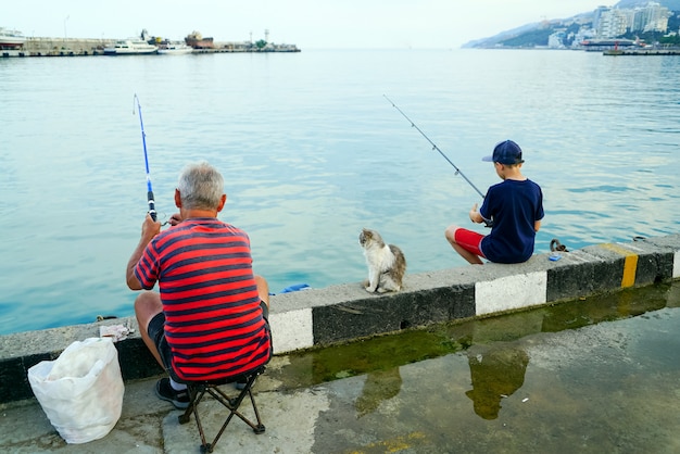 写真 海の桟橋から釣り竿を持つ少年と祖父。