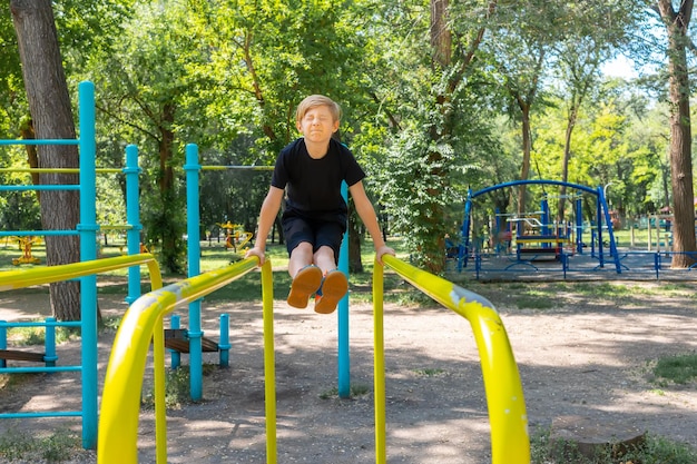 The boy athlete performs an exercise on the gymnastic bars while he stretched his legs forward and twisted his face from the fact that it is very difficult for him to perform this exercise