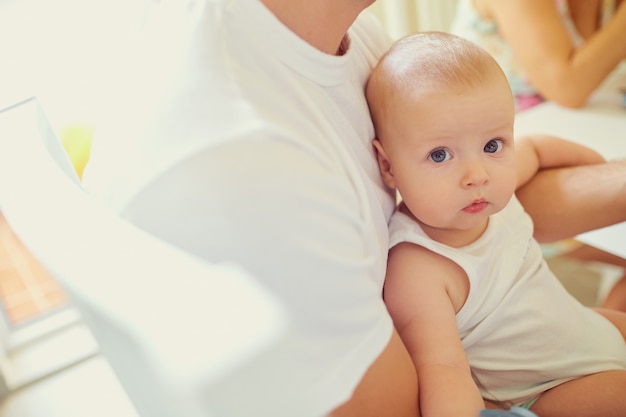 カメラを見ている彼の父の腕の中で男の子の赤ちゃん