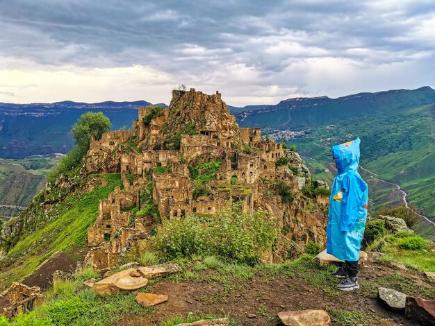 A boy on the background of Gamsutl village in the Caucasus mountains on top of a cliff Dagestan Russia June 2021