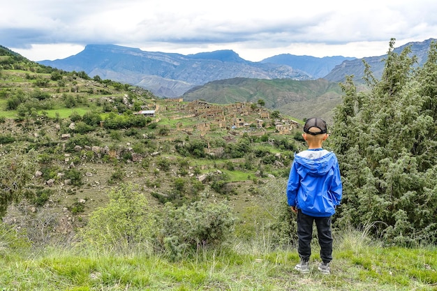 A boy on the background of the village of Kurib in the Caucasus mountains on top of a cliff Dagestan Russia June 2021