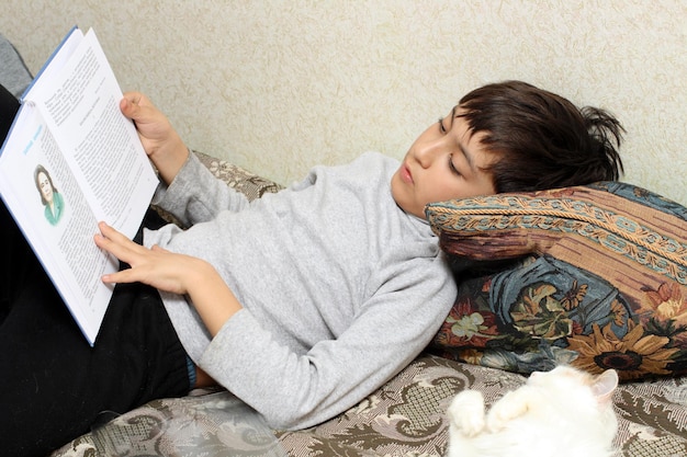 Photo boy on bed with cat reading bok