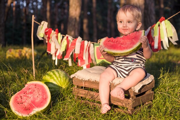 Boy blond sits surrounded by watermelons on a summer day