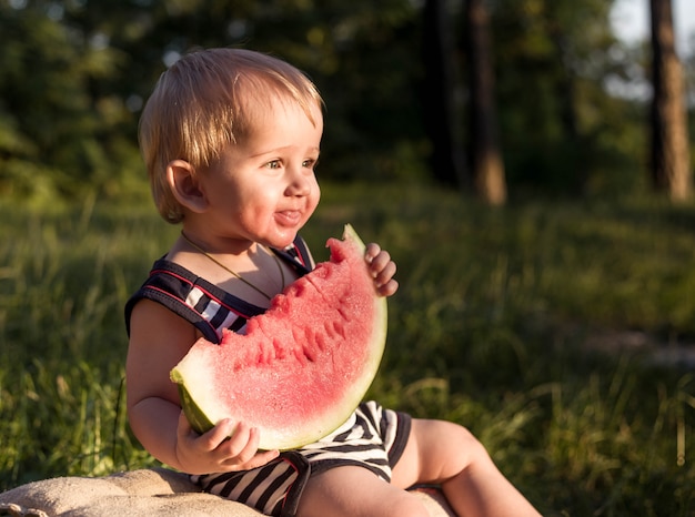 夏の日にスイカに囲まれて金髪の少年が座っています。