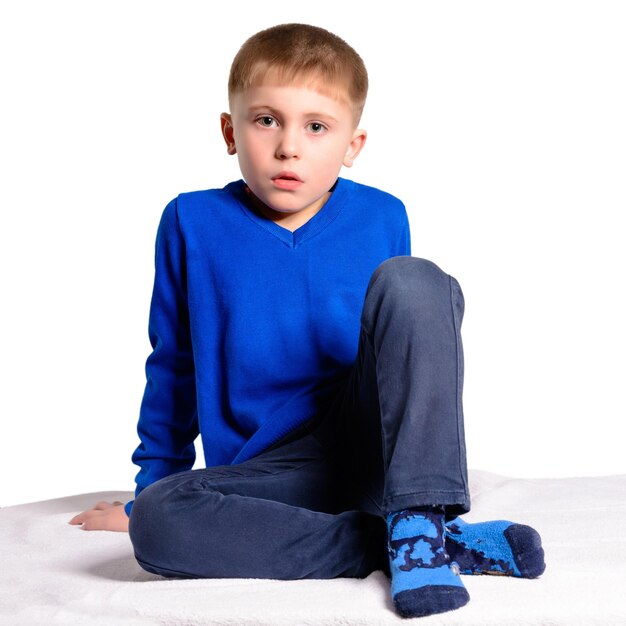 A boy in a blue jacket sits isolated on a white background