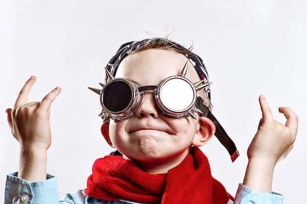 Boy in blue shirt, red scarf, biker glasses and bandana on light background