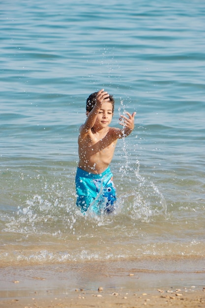 A boy in blue shorts splashes in the water at the beach.