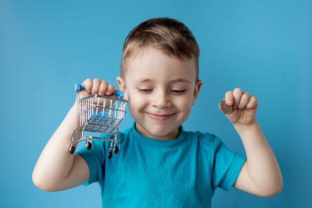 Boy in blue t-shirt is holding shopping cart and coin on blue