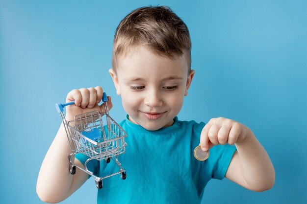 Boy in blue t-shirt is holding shopping cart and coin. Shopping and sale concept.