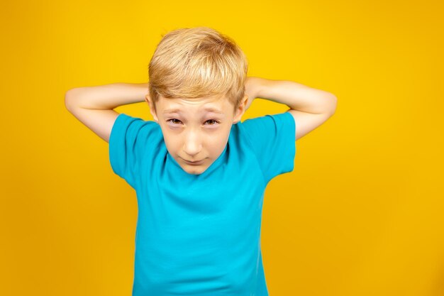 Boy in a blue tshirt on a yellow background raised his hands above his head