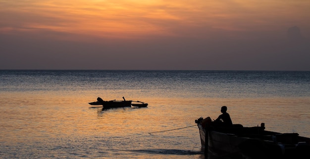 Un ragazzo in una barca guarda il tramonto su zanzibar tanzania africa