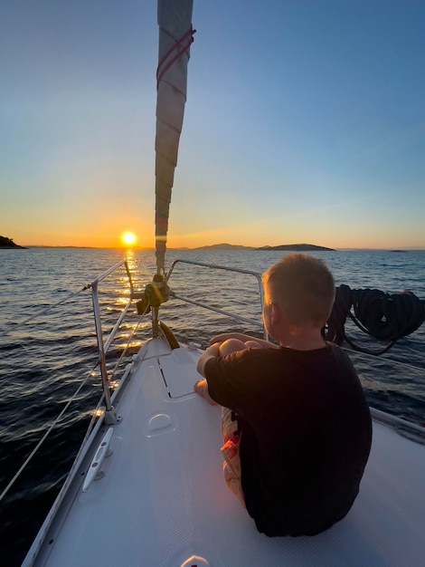 a boy on a boat with the sun setting behind him