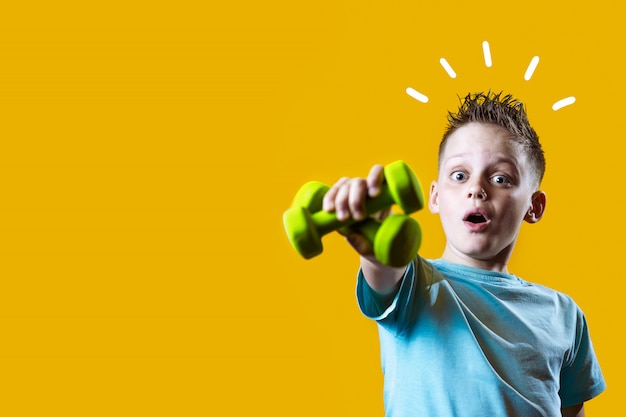 A boy in a bright t-shirt with dumbbells on a yellow background