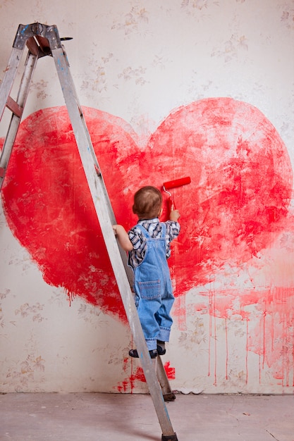 A boy a bucket stand on a ladder paint the wall in red, a big heart.