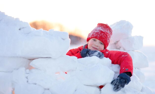 少年は雪で要塞の壁を作り、カメラを見て笑顔で幸せで疲れました