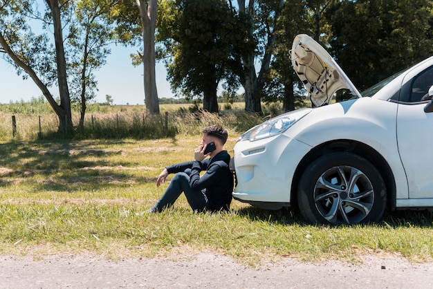 壊れた車の隣に電話する男の子