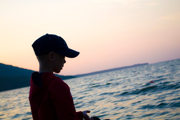 A boy in a cap for walks along the shoreline of the lake psychological rest of children from isolati...