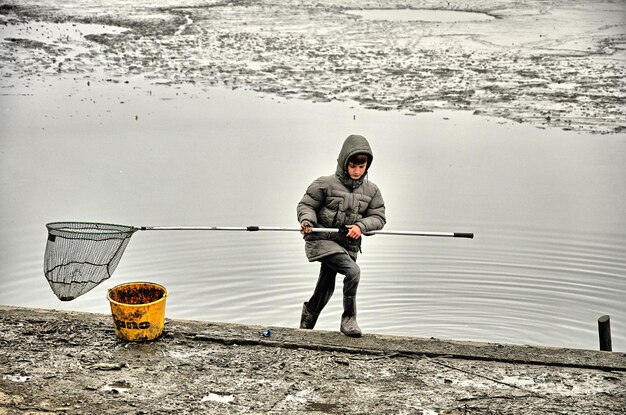 Foto ragazzo che porta la rete da pesca mentre è in piedi nel lago