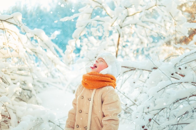 写真 冬の雪の森で雪の結晶を口でキャッチする少年
