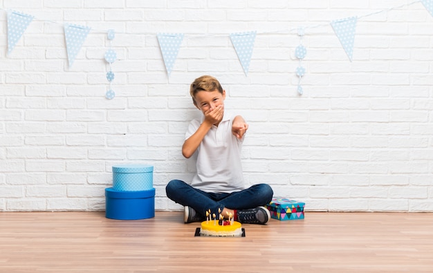 Boy celebrating his birthday with a cake pointing with finger at someone and laughing a lot