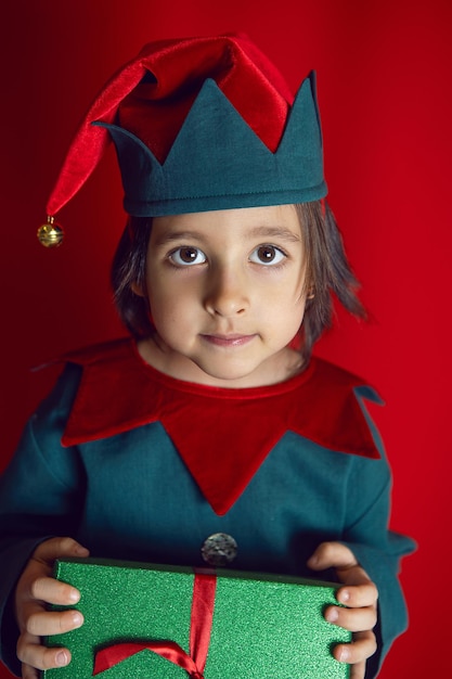 Boy child in a dwarf costume stands on red background on Christmas Day