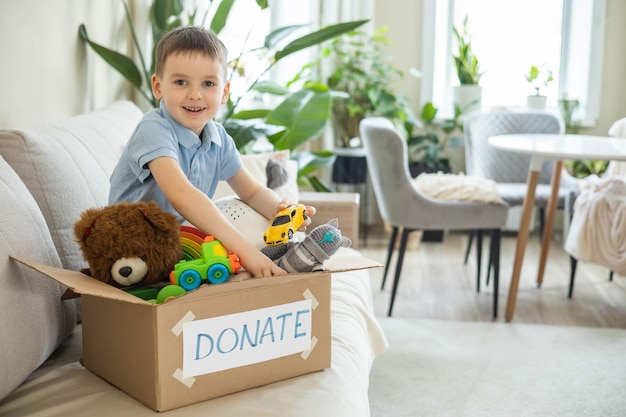 Boy child puts toys in a cardboard box for charity donation concept