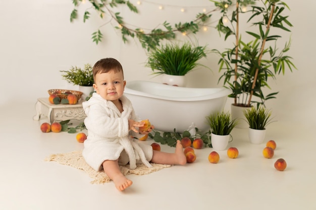 Мальчик сидит возле ванной на белом фоне с персиками и радуется.