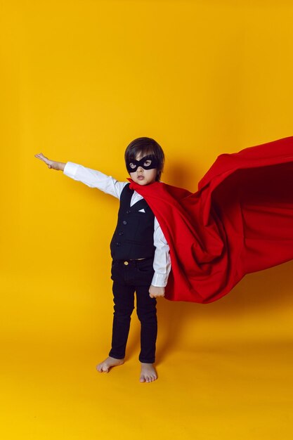 Photo boy child super hero in a suit and black mask in the studio on a yellow background barefoot