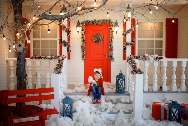 Boy in a Christmas sweatshirt sits on the steps of a house