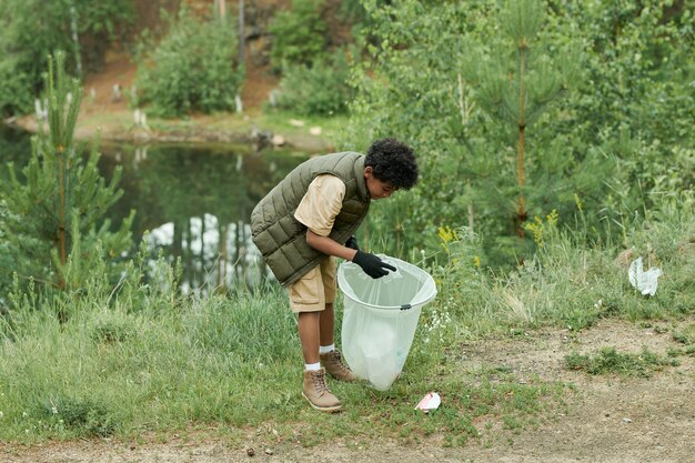 Boy cleaning the territory of forest he putting garbage in bag