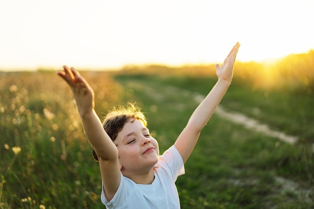 Boy closed her eyes and praying in a field at sunset Hands folded in prayer concept for faith spirituality and religion