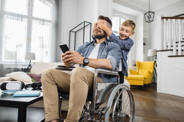 Boy closing disabled fathers eyes from back at home