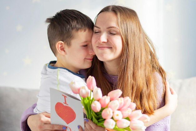 写真 少年が母親を祝い彼女に花チューリップグリーティングカードを贈っています