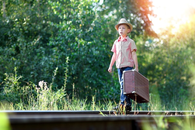 電車と鉄道の西部旅行のコンセプトを待っているスーツケースを持つ少年カウボーイ