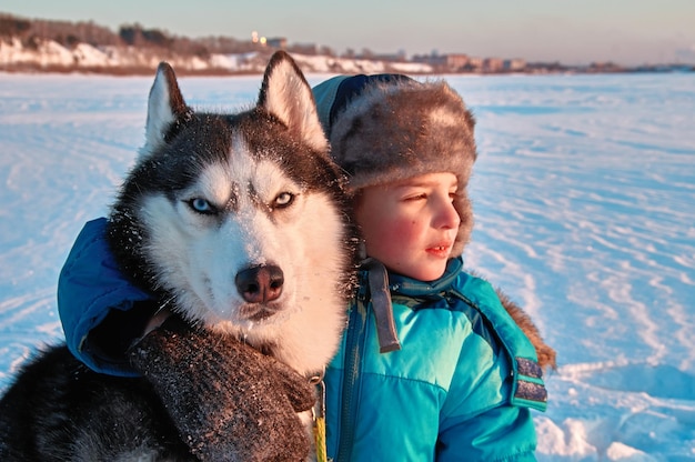 Photo boy cuddles siberian husky dog on winter walk in sunny frosty evening