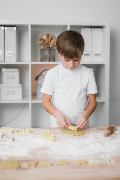 Boy cuts curly cookies from raw dough.